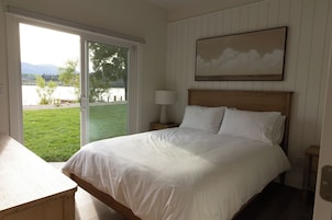 Un dormitorio con cama, mesita de noche, lámpara, un cuadro en la pared y una puerta corrediza de vidrio que da a una zona verde.