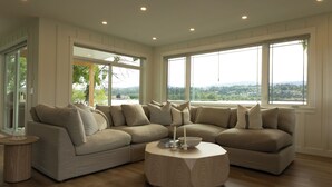 Una sala de estar moderna con un sofá modular, una mesa de centro redonda y ventanas amplias con vistas al paisaje.