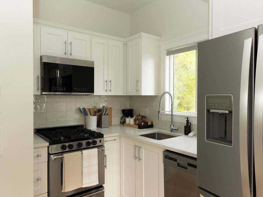 Eine moderne Küche mit weißen Schränken, einem Edelstahl-Kühlschrank, einer eingebauten Mikrowelle und einem Gasherd.