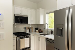 Una cocina moderna con armarios blancos, un refrigerador de acero inoxidable, un microondas integrado y una estufa a gas.
