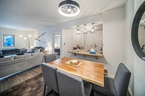 Ein modernes Wohnzimmer mit einer Couch, einem Esstisch mit Stühlen, einer Küchenzeile mit Arbeitsplatte und einem großen Spiegel.