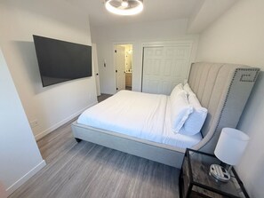 A bedroom with a bed, a TV mounted on the wall, a bedside table with a lamp, and a door leading to a bathroom. - ⛰️ Spacious Mountain Condo | Sleeps 8 guests (Canmore)