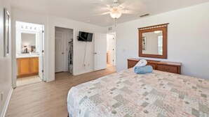 A bedroom with a bed, a ceiling fan, a mirror, and a door leading to a bathroom. - NO HIDDEN FEES! Escape to this comfy 4-bed, 3-bath townhome in gated resort! Relax at the tropical pool with lazy river & waterslide, plus Spa, arcade, gym, business center & dining. Ideal family spot just minutes from all Orlando attractions. (Davenport)