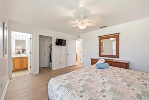 A bedroom with a bed, a ceiling fan, a mirror, and a door leading to a bathroom. - NO HIDDEN FEES! Escape to this comfy 4-bed, 3-bath townhome in gated resort! Relax at the tropical pool with lazy river & waterslide, plus Spa, arcade, gym, business center & dining. Ideal family spot just minutes from all Orlando attractions. (Davenport)