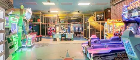 An indoor arcade with various gaming machines, including a 'Lane Master' game, and a climbing wall structure.