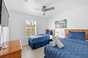 Une chambre avec deux lits, un ventilateur de plafond, une fenêtre avec des stores et un tableau au mur.