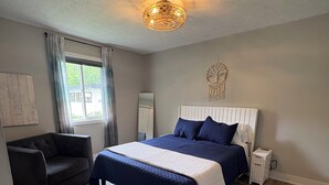 A bedroom with a bed, a bedside table, a nightstand, a chair, a window, and a ceiling light fixture. - Barefoot Boho Bay - Morse - Cicero Indiana (Cicero)