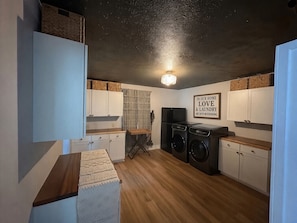 A compact laundry room with two washing machines, a refrigerator, and a wall-mounted sign.