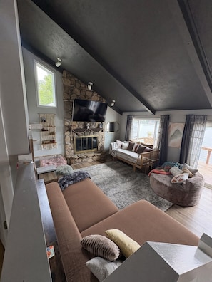 Uma sala de estar aconchegante com lareira de pedra, televisão de tela plana, sofá e janela com cortinas.