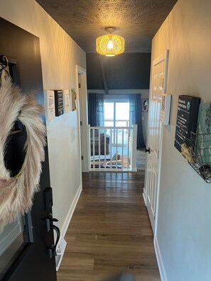 A hallway with a white railing, a hanging decorative item, and a ceiling light fixture.