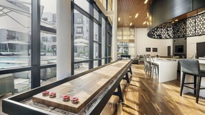 A pool table in a modern indoor setting with large windows, a bar area, and a view of the outside.