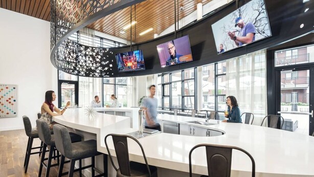 A modern kitchen with a central island, multiple screens, and large windows.