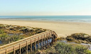 A wooden boardwalk leading to a beach with a clear view of the ocean.