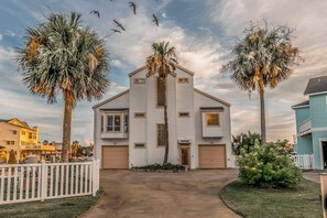 A two-story house with a garage, surrounded by palm trees and a white picket fence. - Waterfront Bunk Retreat w/ Pool, Jamaica Beach (Jamaica Beach)