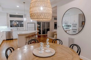 A modern kitchen with white cabinets, a dining area with a round table, and a large mirror on the wall. - Waterfront Bunk Retreat w/ Pool, Jamaica Beach (Jamaica Beach)