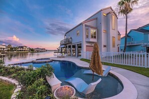 A waterfront property with a swimming pool, a fire pit, and a white picket fence.