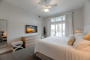 A bedroom with a bed, a ceiling fan, a window with curtains, a bedside table, and a painting on the wall. - Waterfront Bunk Retreat w/ Pool, Jamaica Beach (Jamaica Beach)