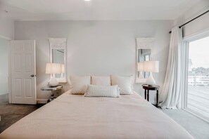 A hotel room with a large bed, two bedside tables with lamps, a mirror, and a view of the city through a window. - Waterfront Bunk Retreat w/ Pool, Jamaica Beach (Jamaica Beach)