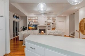 A modern living room with a fireplace, white furniture, and a large white island.