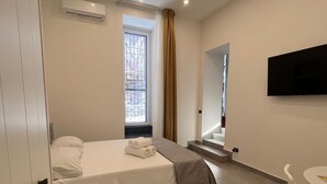 A bedroom with a bed, a TV, a window, and a staircase. - IN THE HEART OF CATANIA — THE PETITE SUITE SAN GIULIANO (Catania)