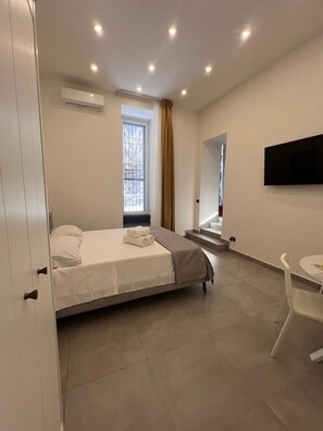Ein Schlafzimmer mit Bett, Fernseher, Fenster und einer Treppe.