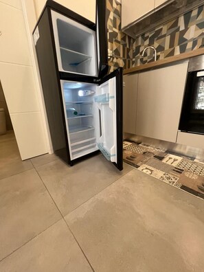 Eine Küche mit Kühlschrank, ornamentalem Rückspritzschutz und Fliesenboden.