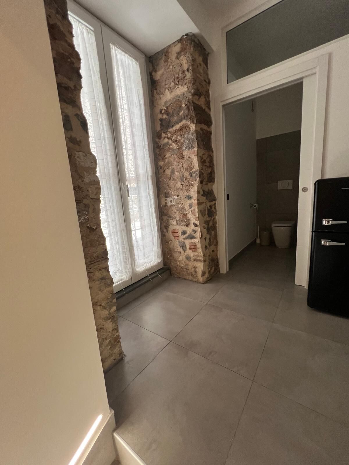 Ein Zimmer mit einer Steinsäule, einer Tür zu einem Badezimmer und einem Kühlschrank.