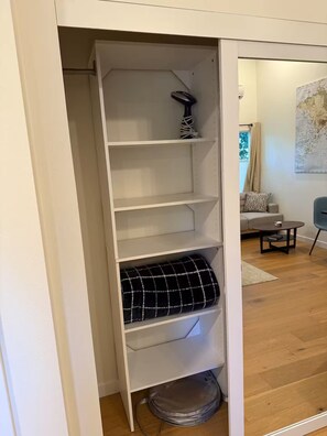 A white shelving unit with a black and white checkered pillow on the bottom shelf.