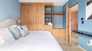 Un dormitorio con cama, armario de madera, estante con toallas y puerta que da a otra habitación.