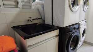 Un espace buanderie comprenant un lave-linge, un sèche-linge, un évier et une fenêtre avec des stores.