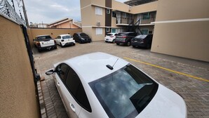 Un parking avec plusieurs voitures, un immeuble à étages et un ciel dégagé.