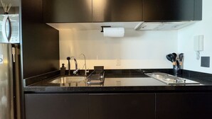 Una cocina moderna con armarios oscuros, un refrigerador de acero inoxidable, horno empotrado y encimera negra.