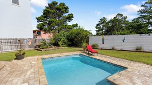 A rectangular swimming pool with a brick deck, surrounded by a wooden fence and a grassy area. - Shore Beats Work - Gulf Views, Pool, Elevator, Beach Access (Panama City Beach)