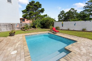 A rectangular swimming pool with a brick deck, surrounded by a wooden fence and a grassy area. - Shore Beats Work - Gulf Views, Pool, Elevator, Beach Access (Panama City Beach)