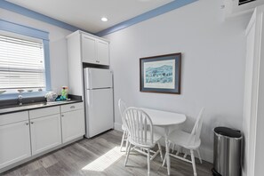 A kitchen with white cabinets, a white refrigerator, a dining table with white chairs, and a framed picture on the wall. - Shore Beats Work - Gulf Views, Pool, Elevator, Beach Access (Panama City Beach)