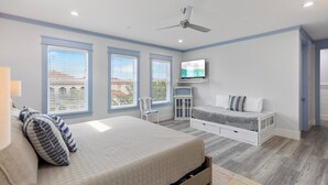 A bedroom with a bed, a TV, a ceiling fan, and large windows. - Shore Beats Work - Gulf Views, Pool, Elevator, Beach Access (Panama City Beach)