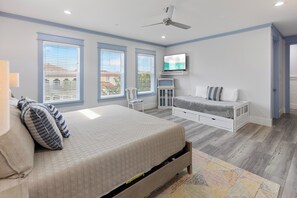 A bedroom with a bed, a TV, a ceiling fan, and large windows. - Shore Beats Work - Gulf Views, Pool, Elevator, Beach Access (Panama City Beach)