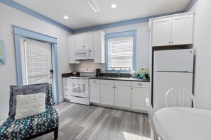A compact kitchen with white cabinets, a built-in microwave, a stove, and a refrigerator. - Shore Beats Work - Gulf Views, Pool, Elevator, Beach Access (Panama City Beach)
