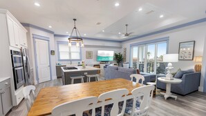 A modern kitchen with a dining area, a living room with a sofa and a TV, and a balcony with a view. - Shore Beats Work - Gulf Views, Pool, Elevator, Beach Access (Panama City Beach)