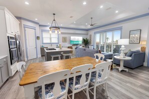 A modern kitchen with a dining area, a living room with a sofa and a TV, and a balcony with a view. - Shore Beats Work - Gulf Views, Pool, Elevator, Beach Access (Panama City Beach)