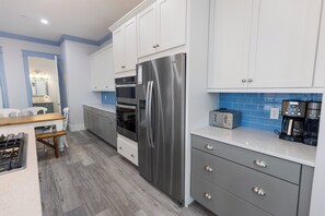 Eine moderne Küche mit weißen Schränken, Edelstahlgeräten, einer Holz Arbeitsplatte und einer blauen Spritzschutzwand.