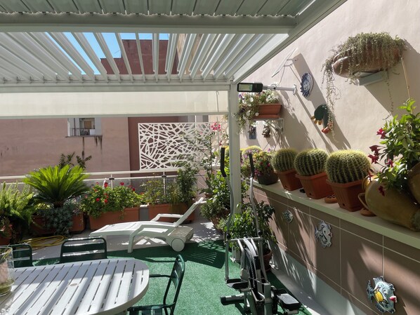 A covered outdoor area with a table and chairs, potted plants, and exercise equipment.