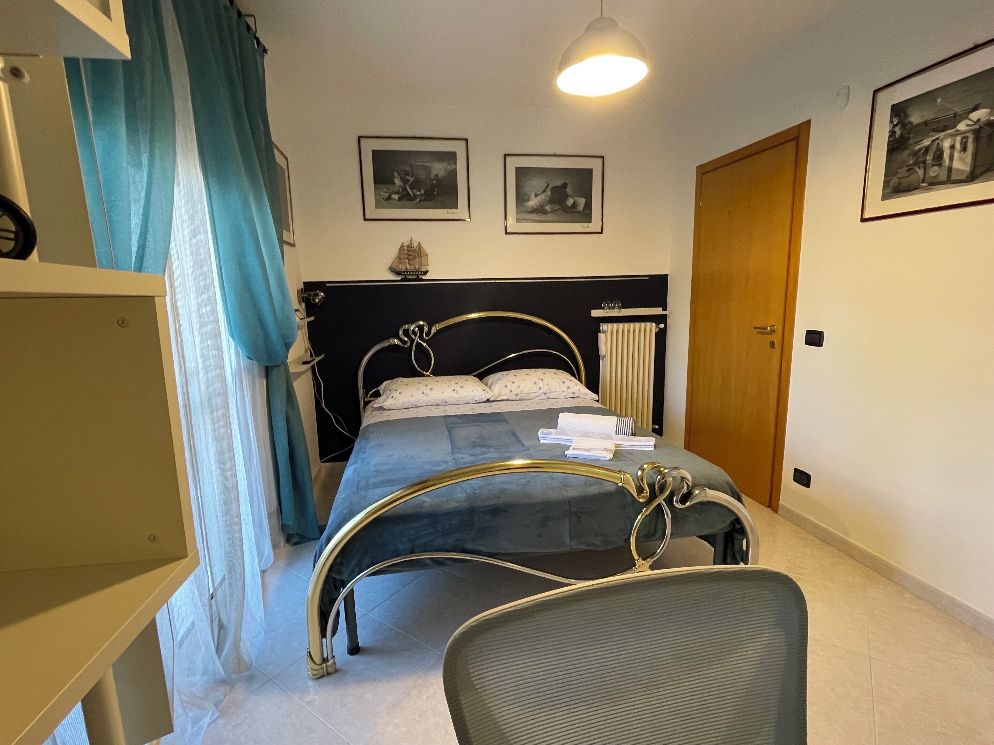 Ein Schlafzimmer mit Bett, Stuhl, Kleiderschrank, einer Tür und zwei gerahmten Bildern an der Wand.