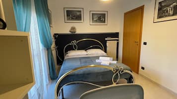 Ein Schlafzimmer mit Bett, Stuhl, Kleiderschrank, einer Tür und zwei gerahmten Bildern an der Wand.