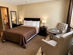 A hotel room with a large bed, two bedside tables with lamps, a round table with a chair, and a mirror on the wall.
