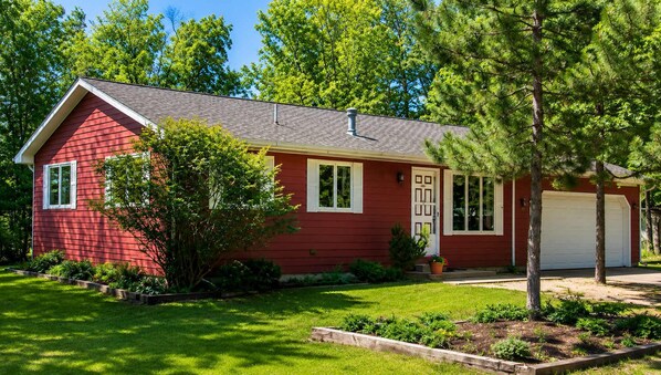 Ein rotes, eingeschossiges Haus mit Garage, umgeben von einem gepflegten Rasen und Bäumen.