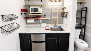 Una cocina compacta con microondas, tostadora, fregadero y armarios negros.