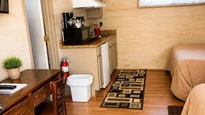 Ein kompakter Raum mit Küchenzeile, Schreibtisch mit Stuhl, Bett und einem gemusterten Teppich.