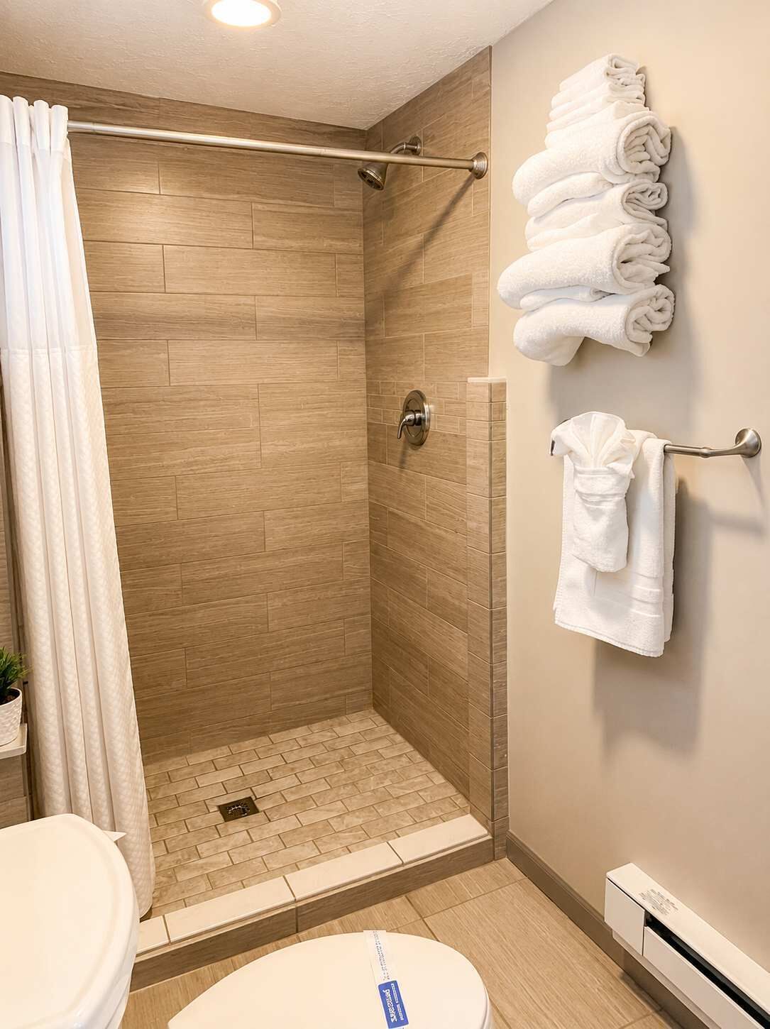 A shower with a glass door, a towel rack with folded towels, and a toilet with a white lid.