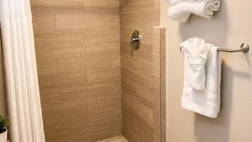 A shower with a glass door, a towel rack with folded towels, and a toilet with a white lid.